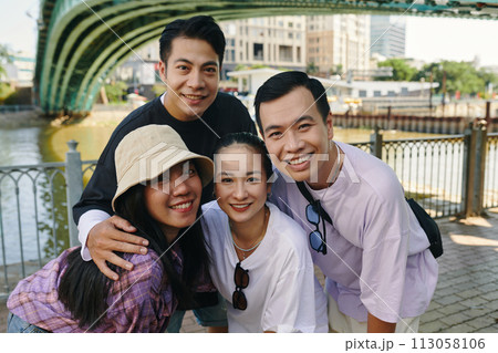 Smiling friends hugging and posing for group phone outdoors Smiling friends hugging and posing for group phone outdoors 113058106