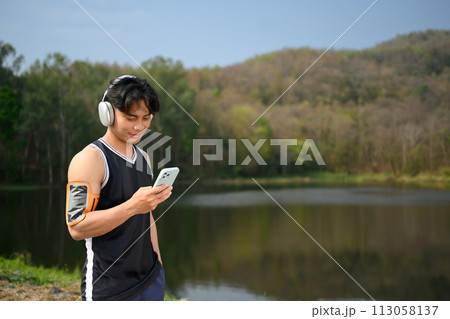 Sportsman listening to music on headphones and using mobile phone at outdoor Sportsman listening to music on headphones and using mobile phone at outdoor 113058137