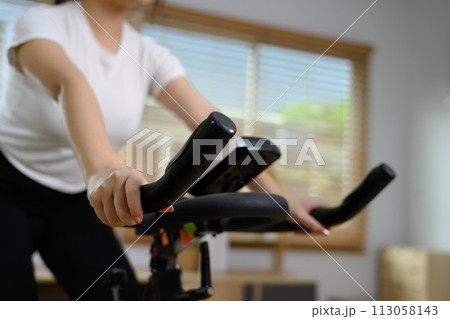 Cropped shot of young woman doing cardio on stationary bike at home 113058143