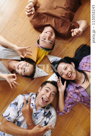 Happy excited friends in birthday hats lying on floor and smiling at camera, top view 113058145