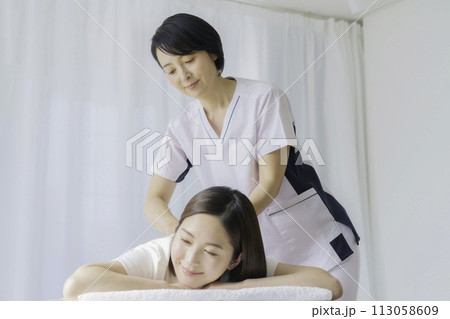 若い女性に施術をするミドルエイジの女性整体師 113058609