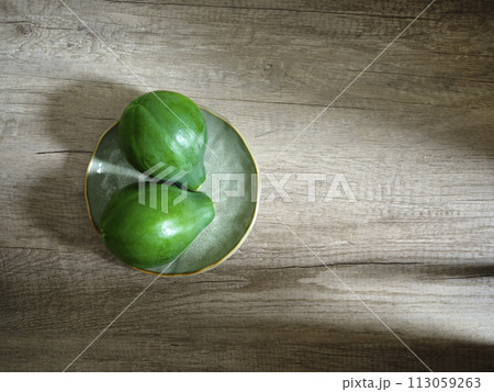two green papayas on plate on wooden surface 113059263