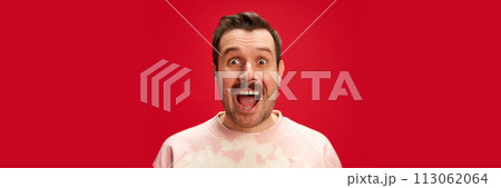 Excited man in tie-dye ping sweatshirt shirt with wide-eyed expression isolated on red studio background. Marketing for unique customer rewards or surprise deals. Excited man in tie-dye ping sweatshirt shirt with wide-eyed expression isolated on red studio background. Marketing for unique customer rewards or surprise deals. 113062064