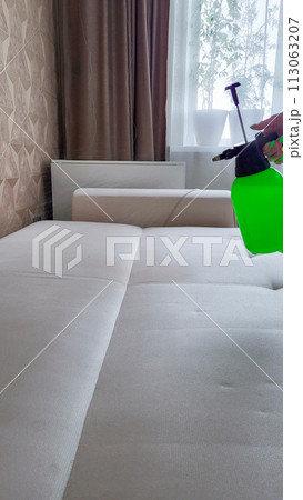 A professional sprays cleaning agent on a white orthopedic sofa to remove stains 113063207
