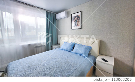interior of the bedroom with a blue bedspread and pillows on the bed, a bedside table 113063209