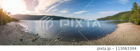 Drone panorama of Loch Ness captures sunlight casting a soft glow over serene lake pebbled beaches Drone panorama of Loch Ness captures sunlight casting a soft glow over serene lake pebbled beaches 113063304