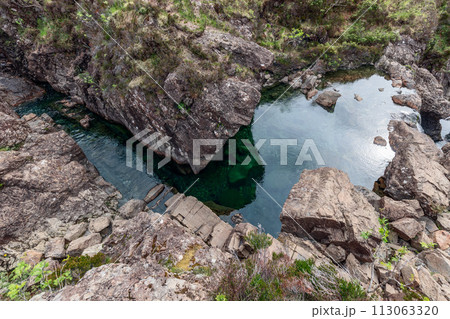 Emerald waters of the Fairy Pools glisten from above, cradled by Isle of Skye rocky nature 113063320