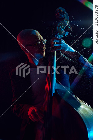 Male musician playing double bass against black background with lights elements. Classical music performance. 113063879