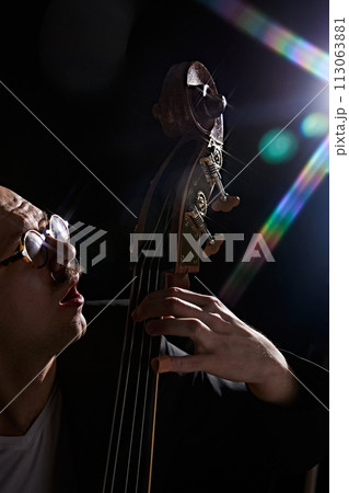 Male musician playing double bass against black background with lights elements. Classical music performance. Male musician playing double bass against black background with lights elements. Classical music performance. 113063881