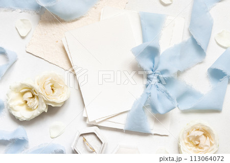 Cards tied with a light blue ribbons near cream roses on white table top view, wedding mockup Cards tied with a light blue ribbons near cream roses on white table top view, wedding mockup 113064072