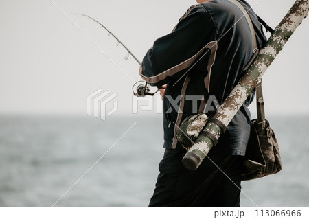 Man hobby fishing on sea tightens a fishing line reel of fish summer. Calm surface sea. Close-up of a fisherman hands twist reel with fishing line on a rod. Fishing in the sea outdoors. Slow motion. 113066966