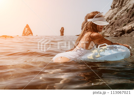 Woman summer sea. Happy woman swimming with inflatable donut on the beach in summer sunny day, surrounded by volcanic mountains. Summer vacation concept. 113067021