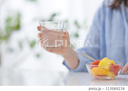 水のグラスを手にフルーツを食べるミドル女性の手元 113068216