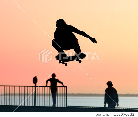 Unrecognizable teenage boy silhouette showing high jump tricks on scooter against 113070532