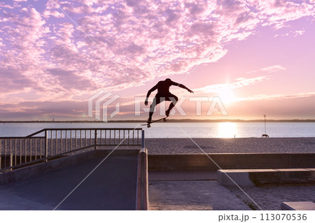 Unrecognizable teenage boy silhouette showing high jump tricks on scooter against Unrecognizable teenage boy silhouette showing high jump tricks on scooter against 113070536