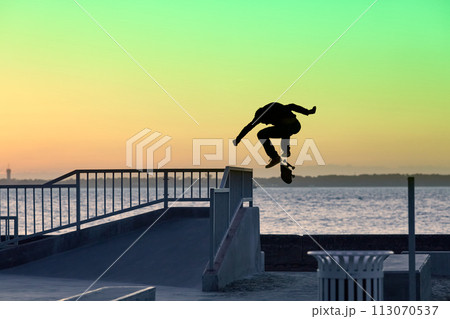 Unrecognizable teenage boy silhouette showing high jump tricks on scooter against 113070537