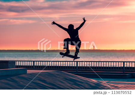 Unrecognizable teenage boy silhouette showing high jump tricks on scooter against 113070552