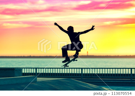 Unrecognizable teenage boy silhouette showing high jump tricks on scooter against Unrecognizable teenage boy silhouette showing high jump tricks on scooter against 113070554