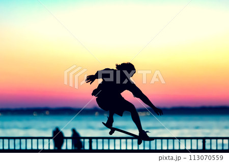 Unrecognizable teenage boy silhouette showing high jump tricks on scooter against 113070559