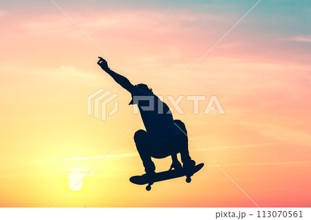 Unrecognizable teenage boy silhouette showing high jump tricks on scooter against 113070561
