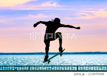 Unrecognizable teenage boy silhouette showing high jump tricks on scooter against 113070566