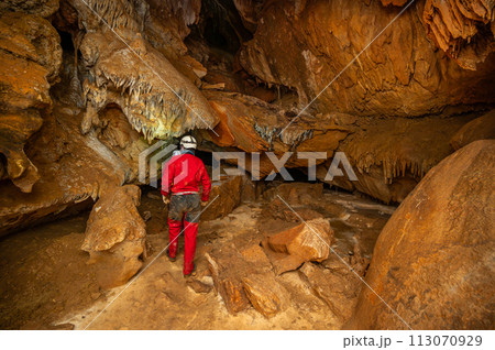 A speleologist with helmet and headlamp exploring a cave with rich stalactite and stalagmite 113070929