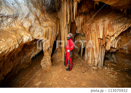 A speleologist with helmet and headlamp exploring a cave with rich stalactite and stalagmite 113070932