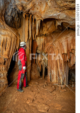 A speleologist with helmet and headlamp exploring a cave with rich stalactite and stalagmite 113071014