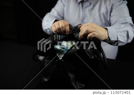 A business man was given a bribe of money dollars in a large bag on a black background. A businessman zips up a bag with a million dollars. Concept of bureaucracy, bribery. A business man was given a bribe of money dollars in a large bag on a black background. A businessman zips up a bag with a million dollars. Concept of bureaucracy, bribery. 113071401