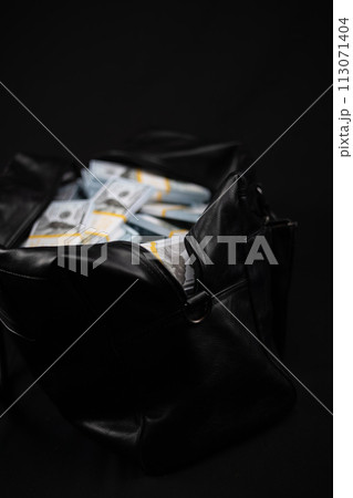 On a black background, a bag full of money. Vertical. Stacks of dollars are folded into a black leather bag on the table. A beautiful bag with a lot of money stands on a table on a black background. On a black background, a bag full of money. Vertical. Stacks of dollars are folded into a black leather bag on the table. A beautiful bag with a lot of money stands on a table on a black background. 113071404