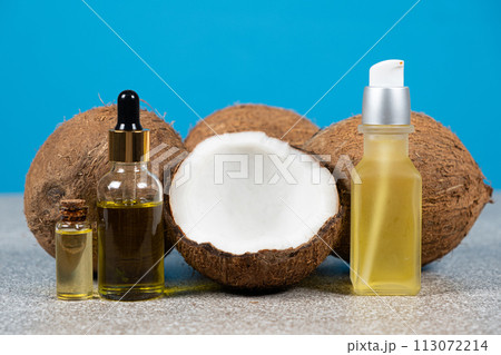 Coconut oil in glass bottles and fruit coconuts on blue background. Coconut oil in glass bottles and fruit coconuts on blue background. 113072214