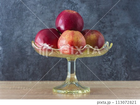 Heap of red apples in a vintage glass vase on a wooden table and gray background Heap of red apples in a vintage glass vase on a wooden table and gray background 113072821