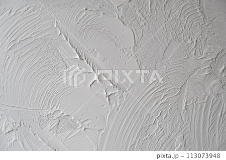 Applying decorative putty. White abstract texture of surface covered with putty. textured background of filler paste applied with putty knife in irregular dashes and strokes. Rough surface plaster 113073948