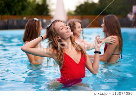Pretty woman in red bikini hanging out with friends at pool party in beach club. Nice girl in one piece swimwear enjoy summer. People have fun swimming in water in luxury private villa swimming pool. Pretty woman in red bikini hanging out with friends at pool party in beach club. Nice girl in one piece swimwear enjoy summer. People have fun swimming in water in luxury private villa swimming pool. 113074086