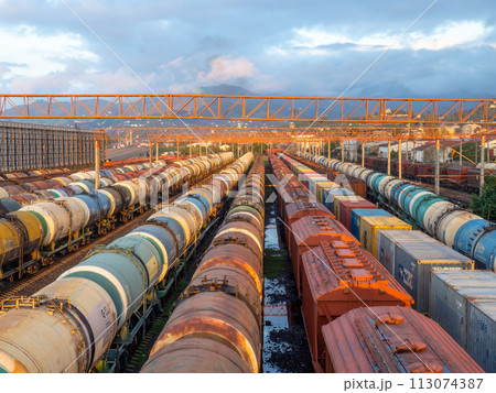 Tanks with fuel on the railway tracks at sunset. Sunset at the train station. The cargo part of the station. industrial zone against the backdrop of mountains. Fuel wagons. Cargo transportation 113074387