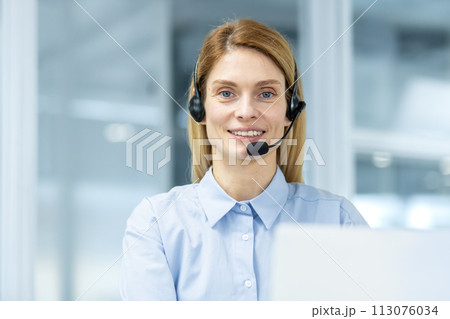 Friendly customer service representative wearing a headset looking at the camera with a confident smile in a modern office setting. Friendly customer service representative wearing a headset looking at the camera with a confident smile in a modern office setting. 113076034