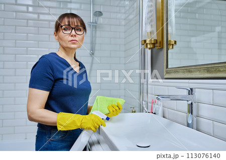 Serious woman with detergent spray, rag cleaning bathroom 113076140