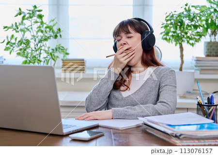 Young female student teenager in headphones yawning covering mouth with hand 113076157