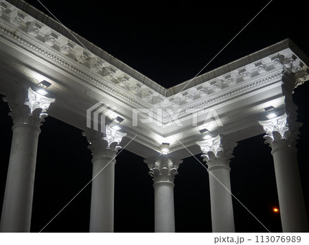White colonnade in the dark. White columns in the light of spotlights. Street decorative architecture. Element of the architectural ensemble in the city park 113076989