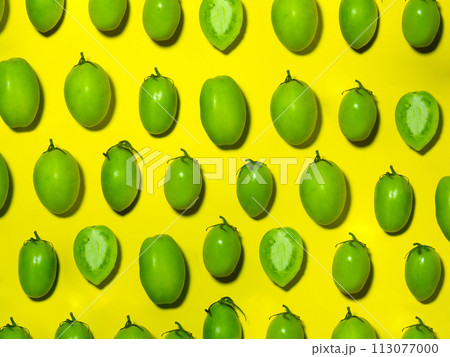 Green tomatoes on a yellow background. The concept of an unripe vegetable. Background from green vegetables. Salting product. 113077000