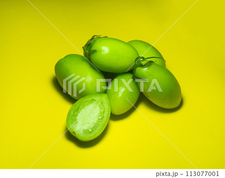 Green tomatoes on a yellow background. The concept of an unripe vegetable.   green vegetables. Salting product. 113077001