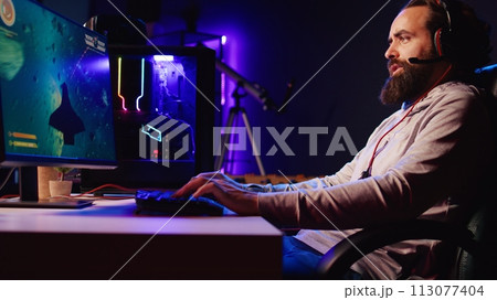 Man in neon lit apartment playing singleplayer videogame with spaceship shooting laser bullets at asteroids. Gamer using crosshair overlay to hit targets in science fiction arcade game, jib down shot 113077404
