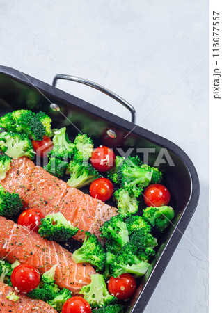 Raw salmon fillet with broccoli and tomato on frying tray, ready to bake, vertical, copy space 113077557
