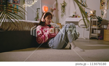 Mongolian girl in headphones surfs social networks using mobile phone Mongolian girl in headphones surfs social networks using mobile phone 113078180