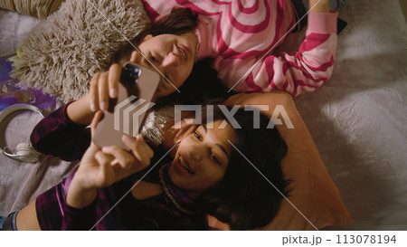 Two multiethnic best friends laugh and scroll through social media using phone Two multiethnic best friends laugh and scroll through social media using phone 113078194
