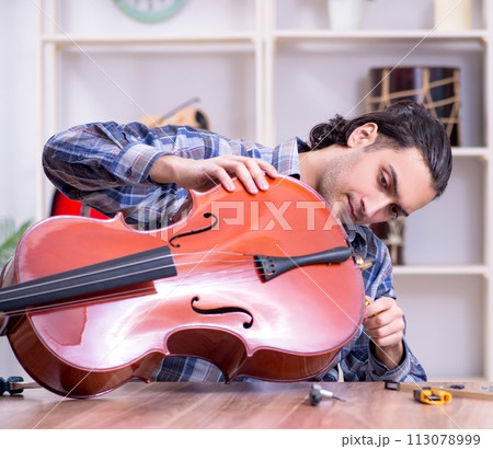 Young handsome repairman repairing cello 113078999