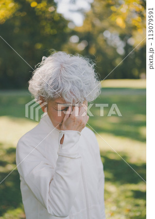 公園の60代女性　眉間を押さえる 113079591