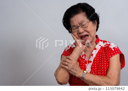 Asia old senior woman suffering from severe toothache, holding her cheek and suffering strong dental pain on white background, tooth decay, tooth sensitivity, oral health care concept. Asia old senior woman suffering from severe toothache, holding her cheek and suffering strong dental pain on white background, tooth decay, tooth sensitivity, oral health care concept. 113079642