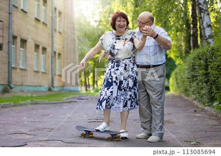 Happy elderly couple with a skateboard. Handsome man and woman senior citizens. Husband and wife of old age for a walk in the city. 113085694