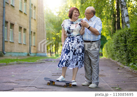 Happy elderly couple with a skateboard. Handsome man and woman senior citizens. Husband and wife of old age for a walk in the city. 113085695